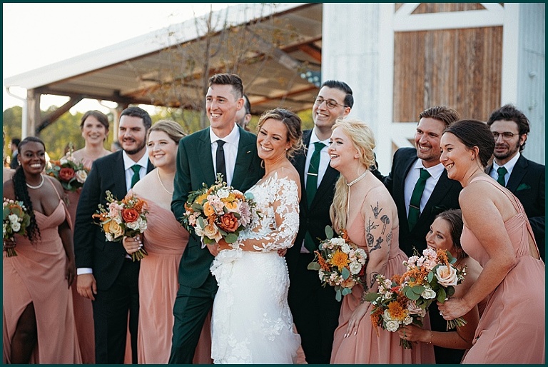 wedding party in blush with warm colored flowers and green suit