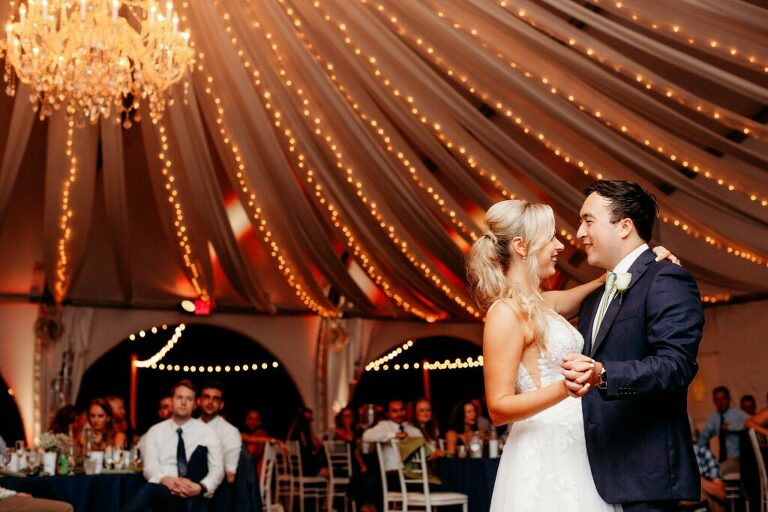 first dance under tent with crystal chandelier at Herrington on the Bay for Annapolis waterfront wedding. Blue suite groom
